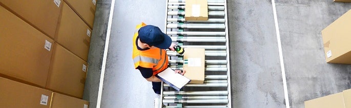 A person in an orange vest holding a clipboard and a cardboard box Description automatically generated