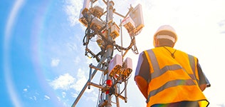 A person in a safety vest and helmet standing next to a tower Description automatically generated