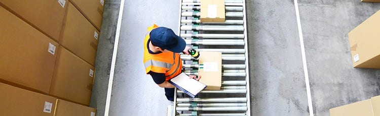 Person with a blue cap and orange vest scanning a package on an assembly line
