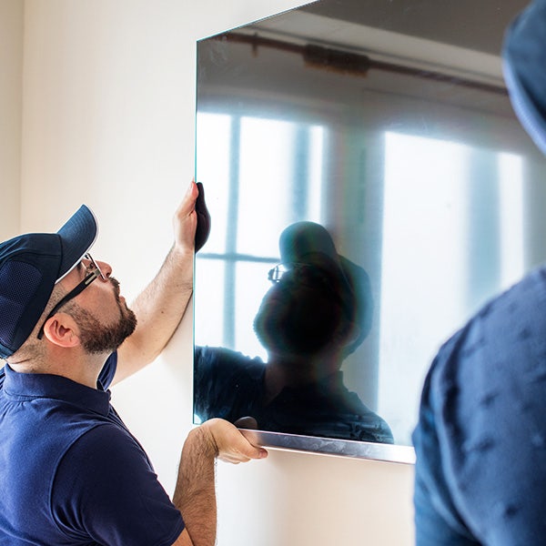 Two men wearing a blue cap and shirt installing a TV