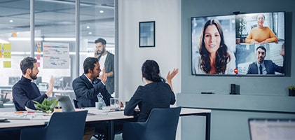 Three people in a conference room waving hi during a virtual meeting